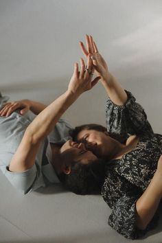 a man and woman laying on the floor with their hands in the air while holding each other