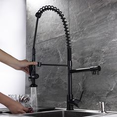 a person washing their hands under a faucet in a kitchen sink with grey marble walls