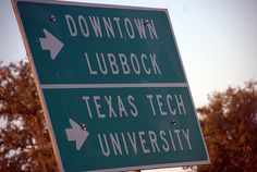 a green street sign with white arrows pointing to downtown and lubbock, texas tech university