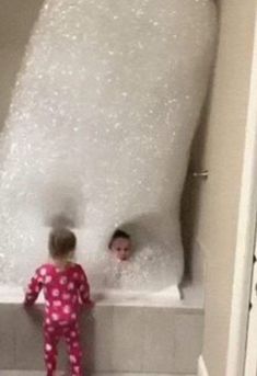 two children are in the bathtub with foam on it and one is wearing pajamas