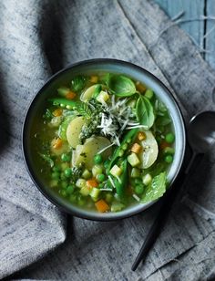 a bowl of vegetable soup on top of a gray cloth next to a silver spoon