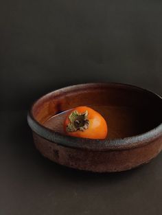 an orange tomato in a brown bowl on a black surface with a knife sticking out of it