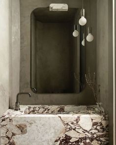 a bathroom sink with marble counter top next to a mirror and two lights hanging from the ceiling