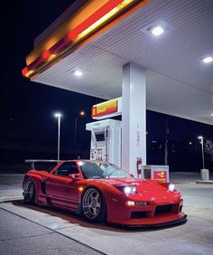 a red sports car parked in front of a gas station at night with its lights on