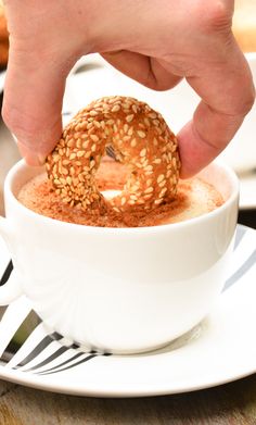 a person is dipping something into a cup filled with hot chocolate and sprinkled with sesame seeds