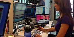 a woman sitting at a desk in front of three computer monitors and a keyboard,