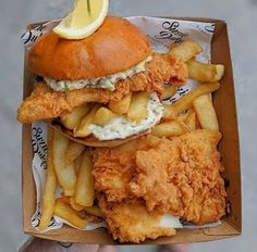 a chicken sandwich with fries and a lemon wedge on top is in a cardboard box