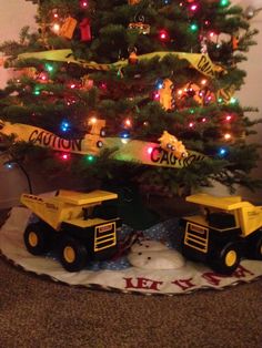 a christmas tree decorated with toys and lights in the shape of dump trucks under it