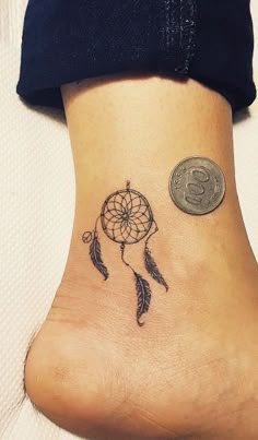 a small tattoo on the ankle of a woman with a dreamcath and coin