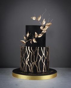 a black and gold wedding cake with leaves on top