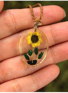 a hand holding a glass pendant with a sunflower in the center and green leaves on it