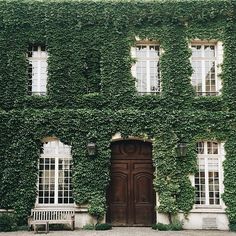 an old building covered in ivy with a wooden door and bench sitting next to it