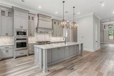 a large kitchen with gray cabinets and white counter tops, hardwood flooring, and two chandeliers