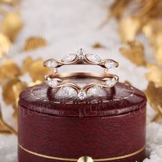 two wedding rings sitting on top of a red velvet ring box with gold leaves in the background