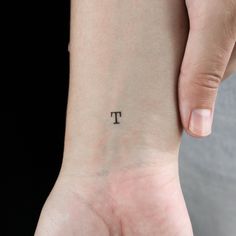 a person with a small tattoo on their left wrist and the letter t is written in black ink