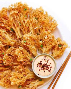 a white plate topped with fried food next to chopsticks and a small bowl