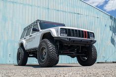 a white jeep is parked in front of a building with a blue wall behind it