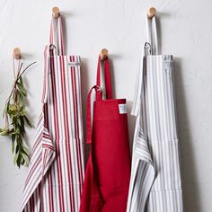 three red and white striped aprons hanging from hooks on the wall next to each other