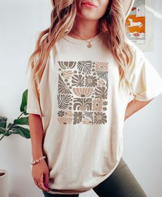 "Retro Boho Wildflowers Ivory Comfort Colors Shirt, Nature Botanical Floral Tee, Cottagecore Wild Flower Neutral Tone T-Shirt, Gift For Her PLEASE SIZE UP FOR AN OVERSIZED FIT If you are looking for an oversized \"T-shirt Dress\" look, we recommend sizing up 2 sizes. Comfort Colors introduces its garment-dyed t-shirt; a fully customizable tee made 100% with ring-spun cotton.  The soft-washed, garment-dyed fabric brings extra coziness to your wardrobe while the relaxed fit makes it an excellent daily choice. The double-needle stitching throughout the tee makes it highly durable while the lack of side-seams helps the shirt retain its tubular shape. .: 100% ring-spun cotton .: Medium fabric (6.1 oz/yd² (206.8 g/m .: Relaxed fit .: Sewn-in twill label" White Crew Neck Tops With Plant Print, Casual Beige Printed Top, Beige Graphic Print Shirt For Summer, White Floral Print Crew Neck Top, Casual Cream Tops With Floral Print, Beige Shirt With Graphic Print For Summer, Casual Cream Floral Print Top, Beige Printed Cotton Shirt, Beige Cotton Printed Shirt