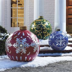 three christmas ornaments sitting on top of snow covered ground in front of a white building