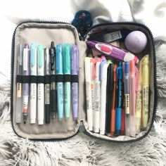 a case filled with lots of different types of pens and pencils next to a stuffed animal