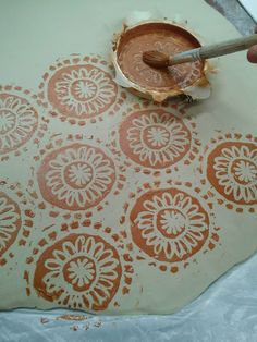 a person using a brush to paint an orange design on a piece of paper that has been cut into smaller circles