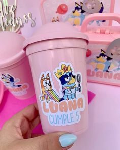 a hand holding a pink cup with cartoon stickers on it and other items in the background