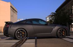 a gray sports car parked on the side of a road next to a train track