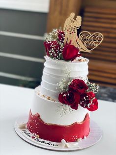 a three tiered wedding cake with red roses and an angel decoration on the top