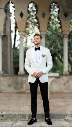 a man in a white tuxedo and black bow tie standing on some steps