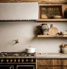 an old fashioned stove in a kitchen with wooden shelves and pots on the top shelf