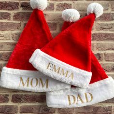 two red and white santa hats with the word emma on them sitting against a brick wall