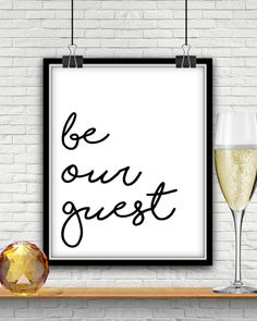 a framed poster with the words be our guest next to two glasses of champagne