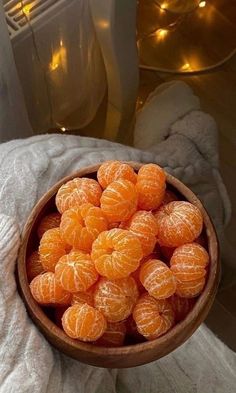 a wooden bowl filled with peeled oranges on top of a white blanket next to candles