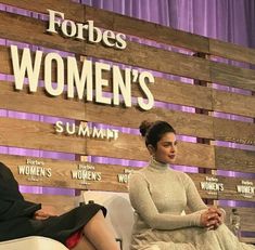 two women sitting on chairs in front of a wooden sign