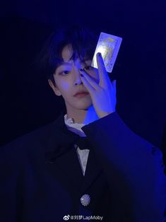 a young man in a tuxedo holds up a card to his face with both hands