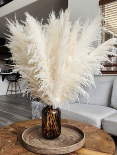 a vase filled with white feathers sitting on top of a wooden table next to a couch