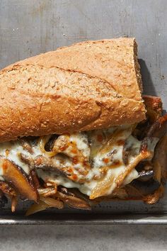 a close up of a sandwich in a pan on a metal surface with meat, cheese and mushrooms