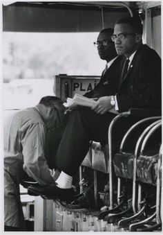 two men in suits are sitting on a bus and one man is reading a book