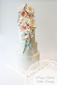 a white wedding cake with flowers on top and lace doily around the edges, sitting on a table