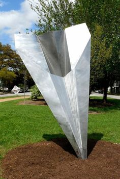 a large metal sculpture sitting in the middle of a field next to a tree and grass