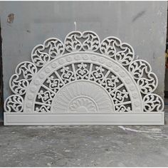 an intricately designed white fireplace screen on the ground in front of a gray wall