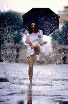 a woman is dancing in the rain with an umbrella and water splashing around her