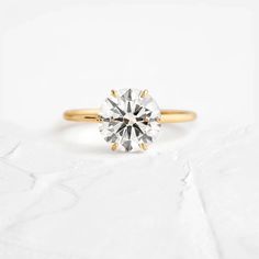 a yellow gold engagement ring with a round brilliant diamond in the center on a white background