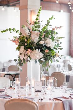 a tall vase filled with lots of flowers on top of a white table cloth covered table