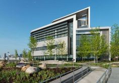 an office building with lots of windows and plants in the foreground on a sunny day