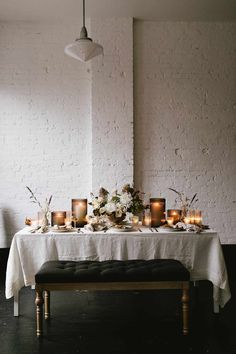 a table with candles and flowers on it in front of a white brick wall, next to a bench