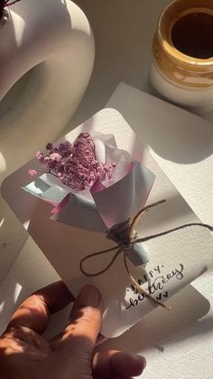 a hand holding a piece of paper with writing on it and some flowers in the background