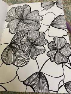 an open notebook with black and white flowers drawn on the pages, next to a purple pen