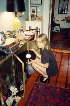 a woman sitting on top of a wooden floor next to a glass case filled with records